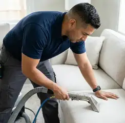 Professional upholstery cleaning technician using an extraction wand to deep-clean a fabric sofa, Fargo, ND.